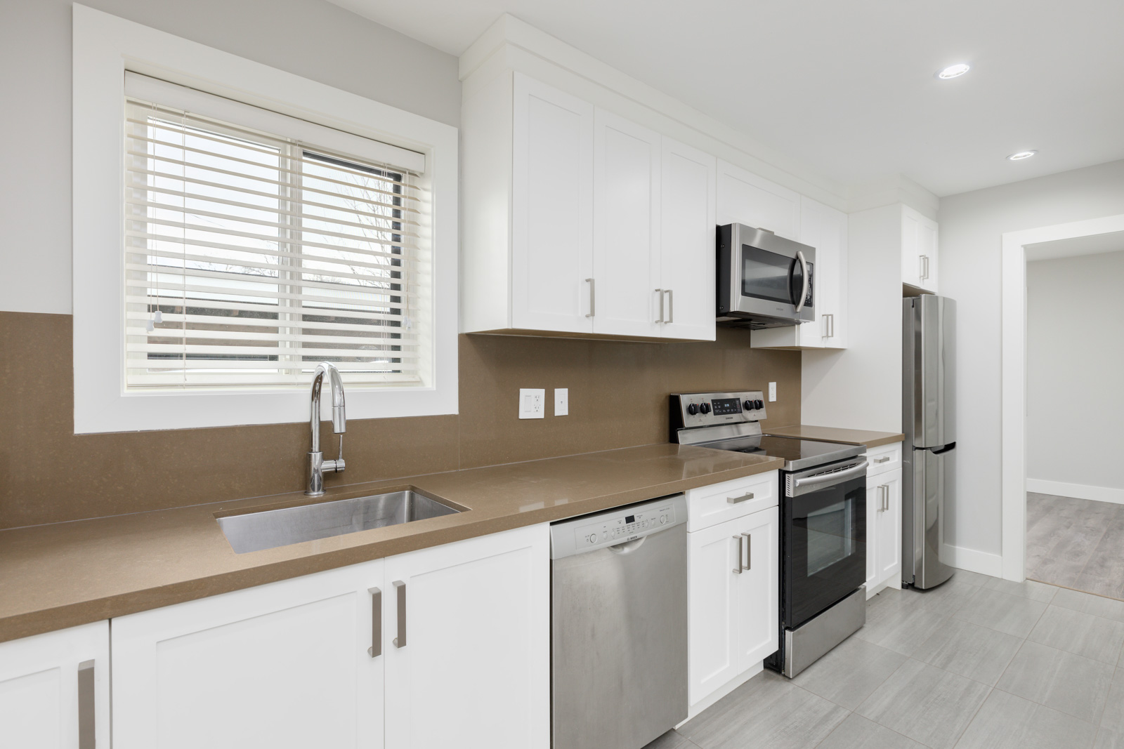 Modern kitchen with white cabinets, stainless steel appliances, a brown countertop, under-mount sink, and a window with blinds above the sink.